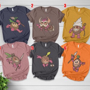 Puede incluir: Seis camisetas de manga corta en varios colores, cada una con un dise&ntilde;o de personaje de dibujos animados. Los personajes tienen una apariencia de coco con diferentes expresiones y accesorios. Las camisetas son azul marino, marr&oacute;n, amarillo mostaza, rosa polvoriento, carb&oacute;n y naranja.