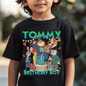 May include: Black t-shirt with a colorful graphic featuring cartoon characters and the text "TOMMY BIRTHDAY BOY". The number "3" is on a birthday cake. The shirt is made of a soft material.