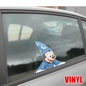 Puede incluir: Una calcoman&iacute;a de vinilo de Mickey Mouse vestido de hechicero, con un sombrero azul con estrellas y una luna creciente. La calcoman&iacute;a est&aacute; en la ventana de un coche, con la palabra "VINYL" en rojo.