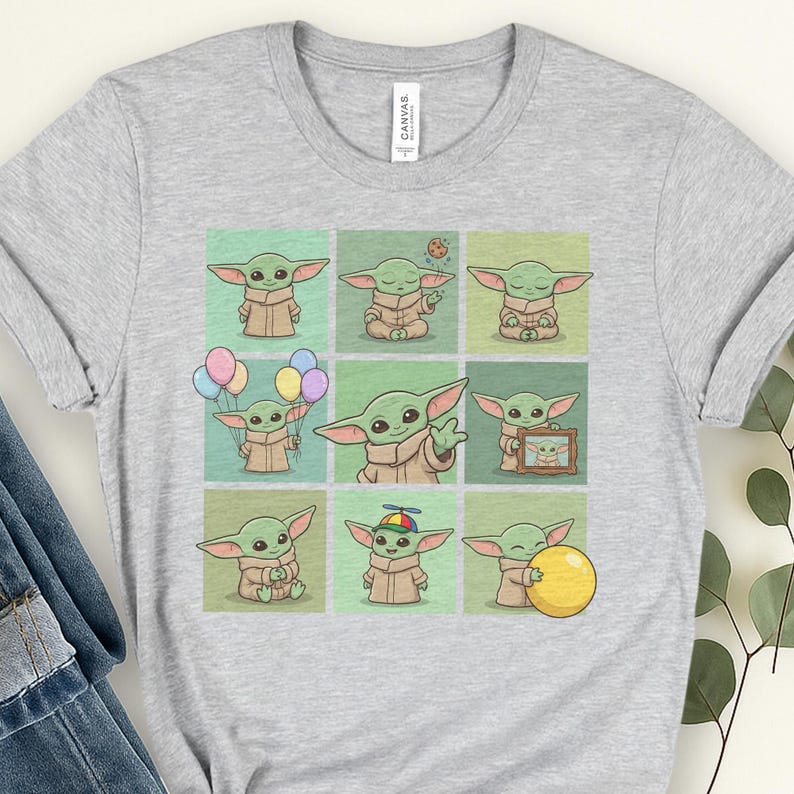 May include: A light grey t-shirt with a grid of nine illustrations of a green alien character. The character is shown in different poses, holding balloons, a biscuit, and a yellow ball. The shirt has a crew neck and short sleeves.