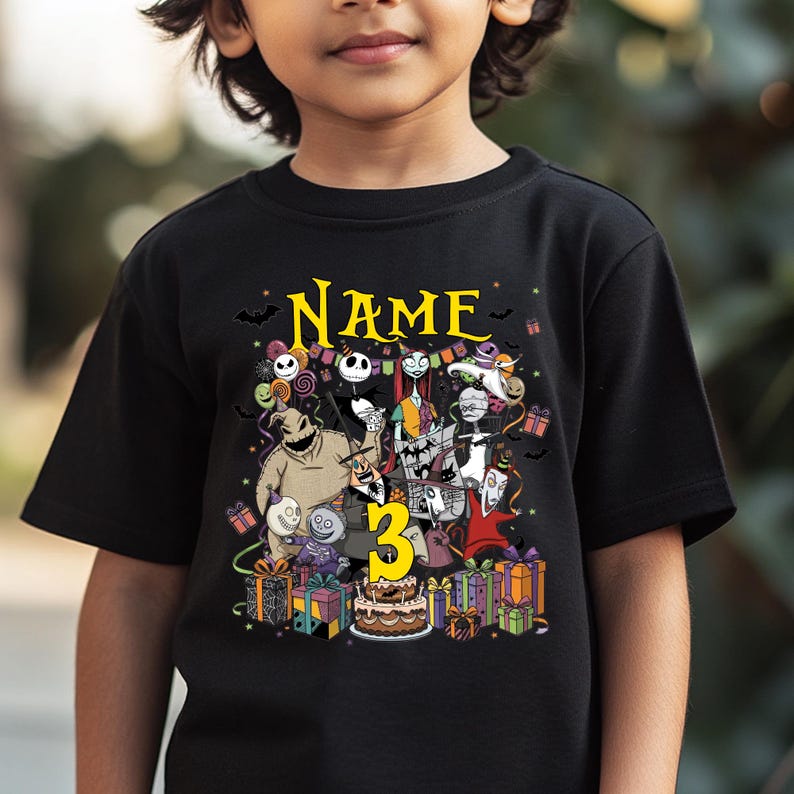 May include: Black t-shirt featuring a colorful graphic of characters from a movie, with the word "Name" in yellow script above the characters and the number "3" in yellow. The shirt is decorated with bats, presents, and a birthday cake.
