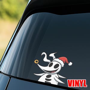 Op de afbeelding: Een witte vinyl sticker met een cartoonfiguur met een rode kerstmuts, een gouden neusring en het nummer 25. Het woord "VINYL" staat in rode blokletters. De sticker is op een autoruit geplakt.
