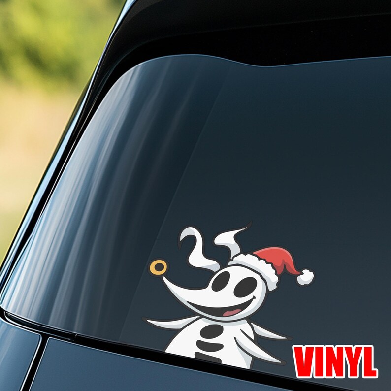 Op de afbeelding: Een witte vinyl sticker met een cartoonfiguur met een rode kerstmuts, een gouden neusring en het nummer 25. Het woord "VINYL" staat in rode blokletters. De sticker is op een autoruit geplakt.