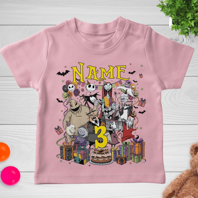 May include: Pink short-sleeved t-shirt featuring a colorful graphic of characters from The Nightmare Before Christmas. The design includes the word "NAME" above the characters and the number "3" in yellow. Presents and a cake are also included.
