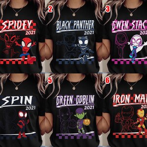 May include: Black t-shirts with superhero graphics. Each shirt has a character's name and "2021" in white or purple text. The designs include Spidey, Black Panther, Gwen Stacy, Spin, Green Goblin, and Iron Man.