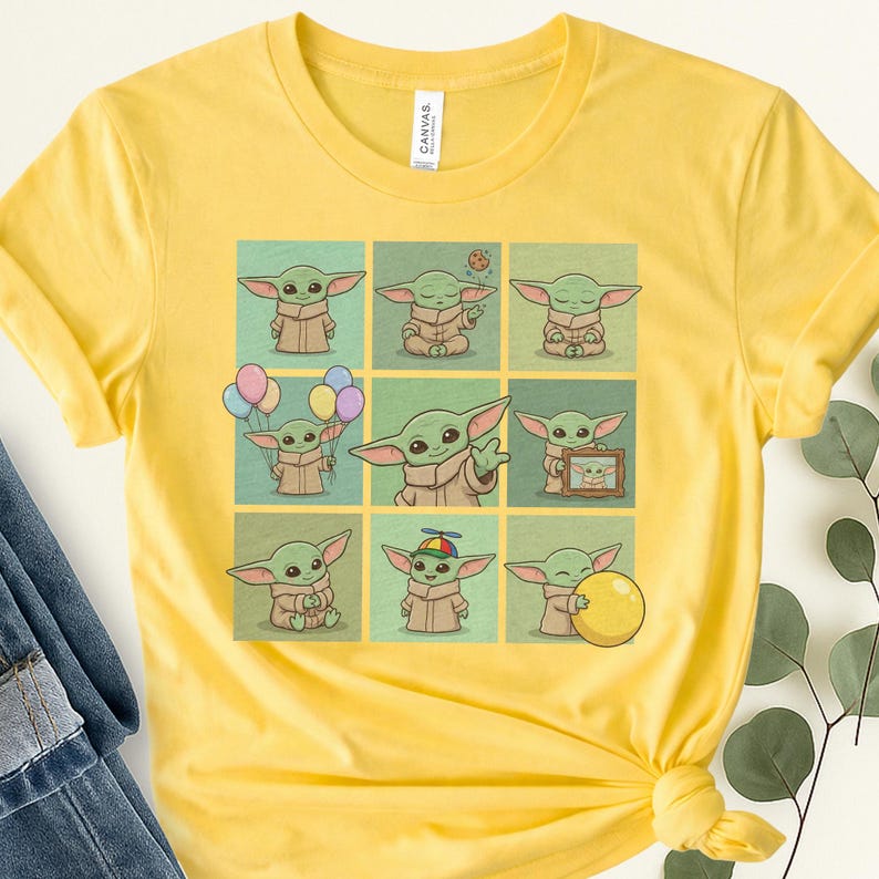 May include: Yellow t-shirt with a grid of nine illustrations of a green alien character in different poses. The character has large ears and a brown robe. The shirt has a crew neck and short sleeves.