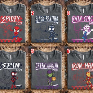 May include: Six grey t-shirts with superhero designs. Each shirt features a different character: Spidey, Black Panther, Gwen Stacy, Spin, Green Goblin, and Iron Man. Each design includes the year 2021.