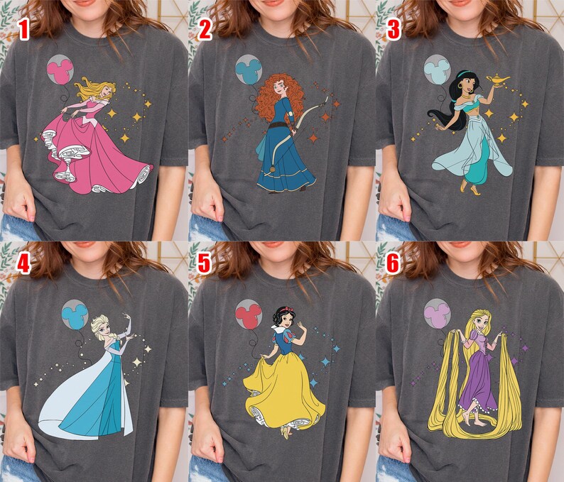 May include: Six dark gray t-shirts with different princess designs. Each shirt features a colorful illustration of a Disney princess, including Aurora, Merida, Jasmine, Elsa, Snow White, and Rapunzel, with a matching balloon.