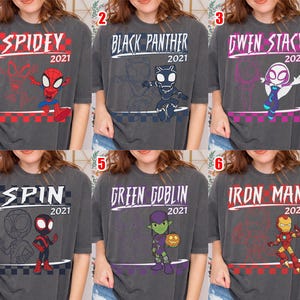 May include: Six charcoal grey t-shirts featuring Marvel characters. Each shirt has a character name and "2021" printed on it. Characters include Spidey, Black Panther, Gwen Stacy, Spin, Green Goblin, and Iron Man.