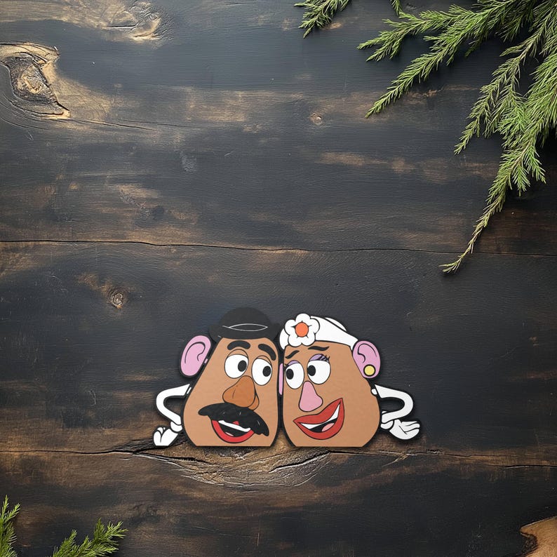 May include: Two cartoon potato head cutouts, one with a black hat and mustache, the other with a white headband and flower. Both have large eyes, pink ears, and red smiling mouths. They are set against a dark wood background with green sprigs.