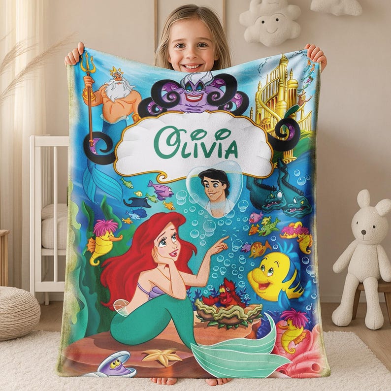 May include: A rectangular fleece blanket featuring a vibrant underwater scene with the name Olivia printed in the center. The design includes characters like Ariel, King Triton, Ursula, Flounder, and Prince Eric, set against a blue ocean background.