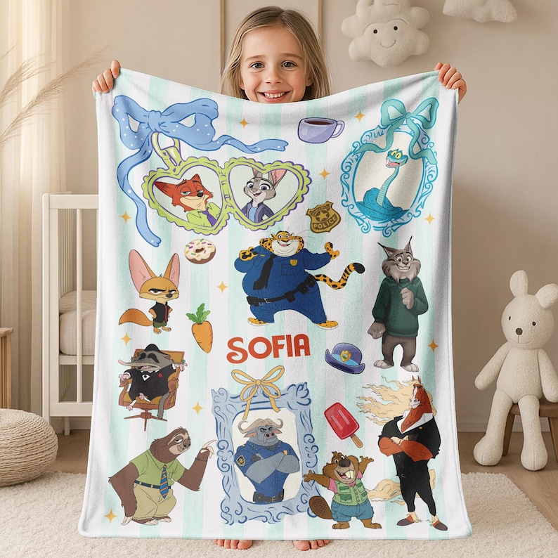Puede incluir: Una manta blanca con un fondo a rayas azul claro con personajes de dibujos animados de Zootopia. La manta incluye im&aacute;genes de Nick Wilde, Judy Hopps y otros personajes. El nombre "Sofia" est&aacute; escrito en rojo.