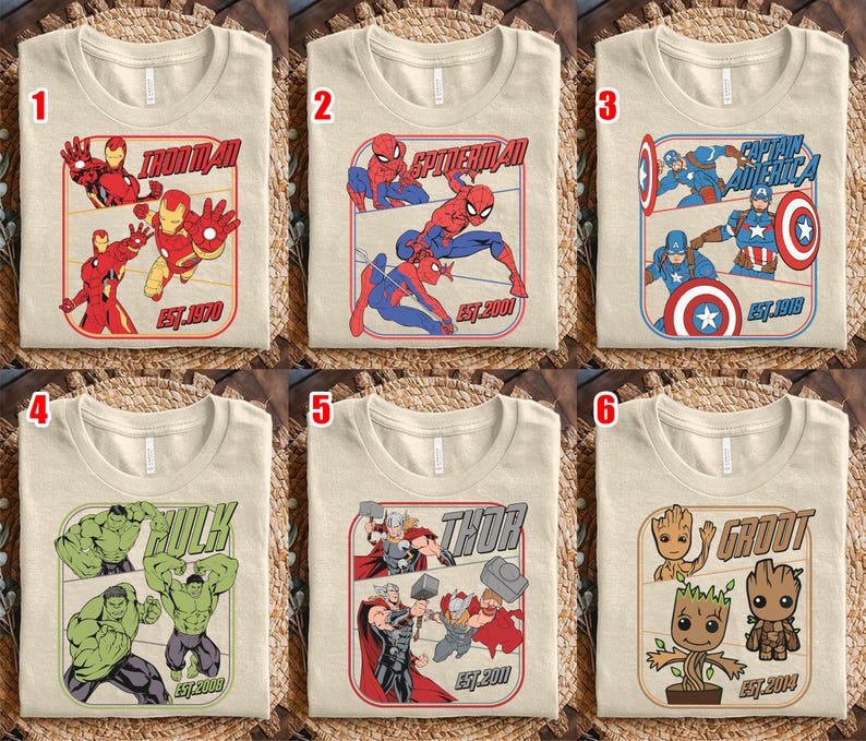 K&ouml;nnte beinhalten: Sechs beige T-Shirts mit Marvel-Superhelden-Grafiken. Jedes Shirt zeigt einen anderen Charakter: Iron Man, Spider-Man, Captain America, Hulk, Thor und Groot. Die Shirts haben den Namen der Figur und das Gr&uuml;ndungsjahr.