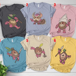 Puede incluir: Una colecci&oacute;n de seis camisetas de varios colores, cada una con un dise&ntilde;o de personaje de dibujos animados. Los dise&ntilde;os representan una criatura parecida a un coco con diferentes accesorios y expresiones. Las camisetas son en tonos de gris, azul, rosa y amarillo.