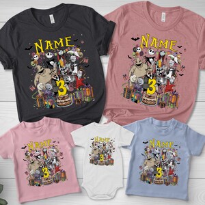 Pode incluir: V&aacute;rias camisetas e um body com um design gr&aacute;fico colorido com personagens, a palavra "Name" e o n&uacute;mero "3". As camisetas s&atilde;o em v&aacute;rias cores, incluindo preto, rosa e azul.