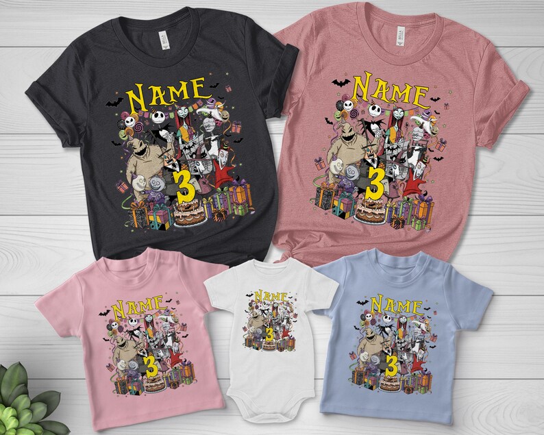 Pode incluir: V&aacute;rias camisetas e um body com um design gr&aacute;fico colorido com personagens, a palavra "Name" e o n&uacute;mero "3". As camisetas s&atilde;o em v&aacute;rias cores, incluindo preto, rosa e azul.