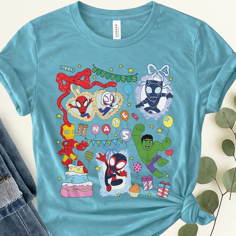 May include: A light blue t-shirt featuring a colorful graphic print of various superheroes, including Iron Man, Hulk, and Spider-Man characters. The design includes a birthday cake, gift boxes, balloons, bunting, and the text NAME 5.