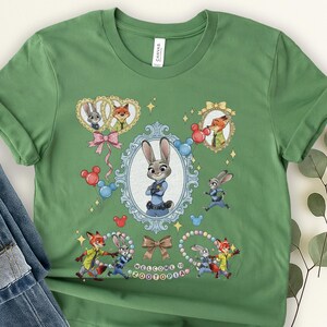 May include: Green t-shirt featuring characters from Zootopia. The design includes Judy Hopps, Nick Wilde, and other characters in oval frames and running. The text "WELCOME TO ZOOTOPIA" is also included.