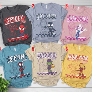 May include: Six t-shirts with Marvel character designs. Each shirt has a character's name and the year 2021, plus a cartoon image. The shirts are in various colours: grey, blue, pink, light blue, beige, and yellow.