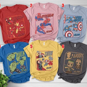 K&ouml;nnte beinhalten: Kollektion von sechs kurz&auml;rmeligen T-Shirts mit Marvel-Comicfiguren. Designs umfassen Iron Man, Spider-Man, Captain America, Hulk, Thor und Groot. Jedes Shirt hat eine Charaktergrafik mit dem Namen der Figur und dem Deb&uuml;tjahr.