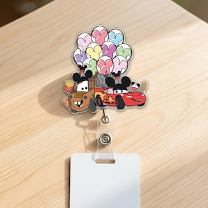 Op de afbeelding: Een kleurrijke badge reel met de tekenfilmfiguren Mater en Lightning McQueen met Mickey Mouse oren, die ballonnen vasthouden. De badge reel heeft een doorzichtige plastic band en een wit rechthoekig label.