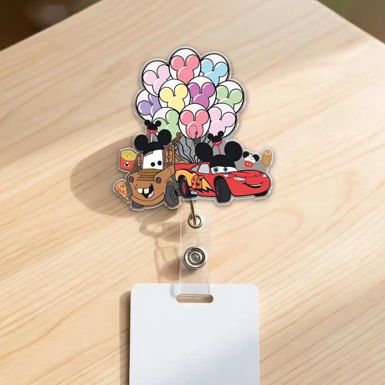 Op de afbeelding: Een kleurrijke badge reel met de tekenfilmfiguren Mater en Lightning McQueen met Mickey Mouse oren, die ballonnen vasthouden. De badge reel heeft een doorzichtige plastic band en een wit rechthoekig label.