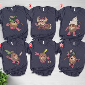 Puede incluir: Seis camisetas azul marino con gr&aacute;ficos de monstruos de dibujos animados. Cada camiseta presenta un dise&ntilde;o de monstruo diferente en tonos de marr&oacute;n, rosa y verde. Los monstruos sostienen varios objetos como lanzas y palos.