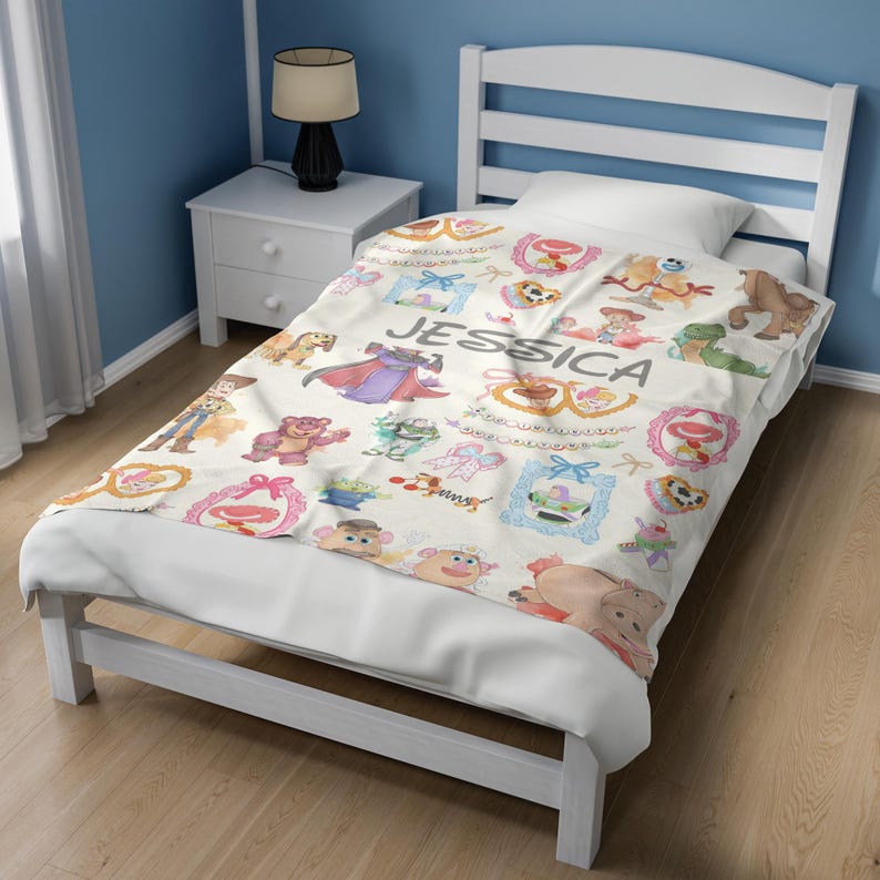 Puede incluir: Una cama individual blanca con una manta con personajes de dibujos animados y el nombre "JESSICA" en letras grises. La manta tiene un patr&oacute;n repetido de varios personajes en marcos y dise&ntilde;os coloridos. El marco de la cama es blanco.