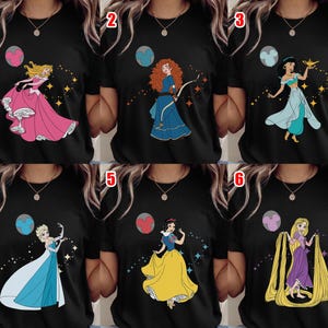May include: Black t-shirts featuring colorful illustrations of animated princesses. Each shirt showcases a different princess, including Aurora in a pink gown, Merida with a bow, Jasmine with a lamp, Elsa in a blue dress, Snow White, and Rapunzel with long hair.