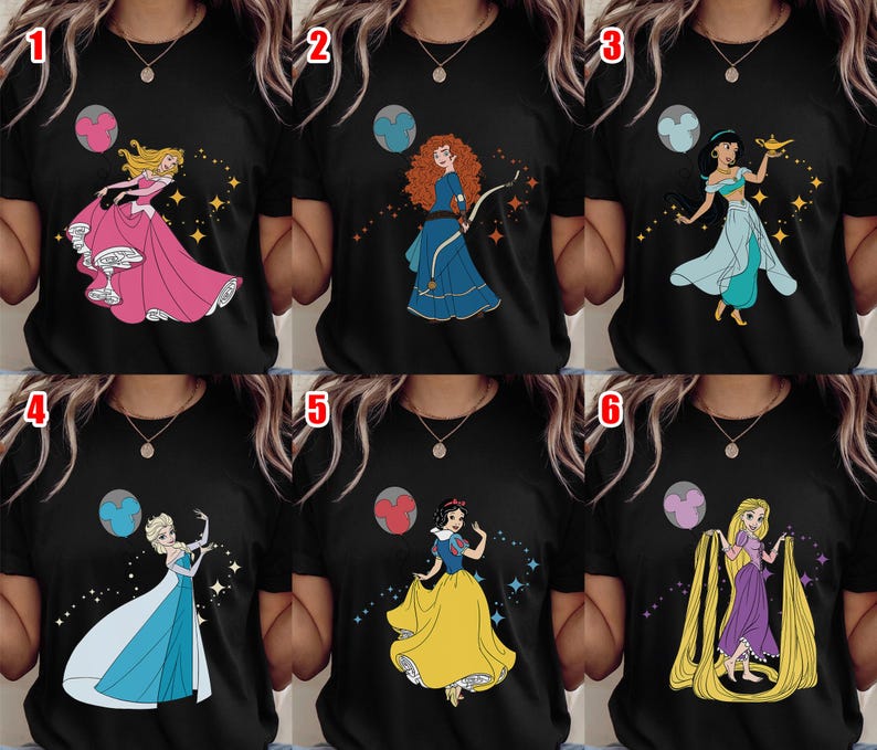 May include: Black t-shirts featuring colorful illustrations of animated princesses. Each shirt showcases a different princess, including Aurora in a pink gown, Merida with a bow, Jasmine with a lamp, Elsa in a blue dress, Snow White, and Rapunzel with long hair.