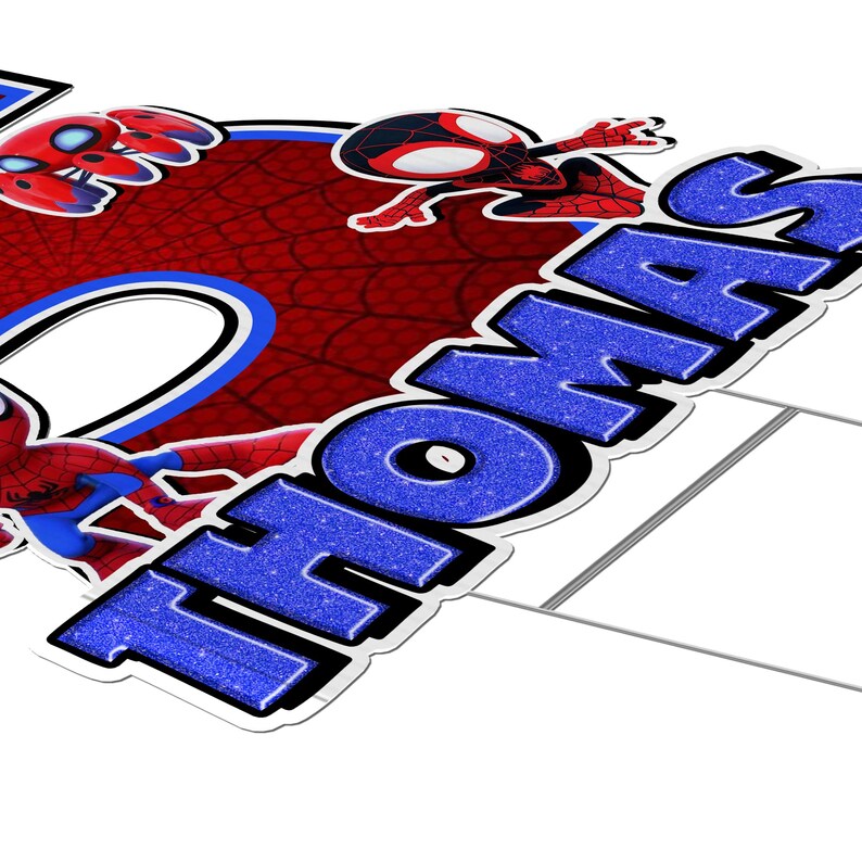 May include: A yard sign featuring the name "THOMAS" in large, glittery blue letters with a black outline. The design includes Spider-Man characters and a red and blue web background.