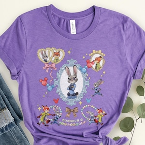 May include: Purple t-shirt featuring characters from the animated film Zootopia. The design includes Judy Hopps, Nick Wilde, and other characters in various poses, surrounded by decorative elements and the text "WELCOME TO ZOOTOPIA".
