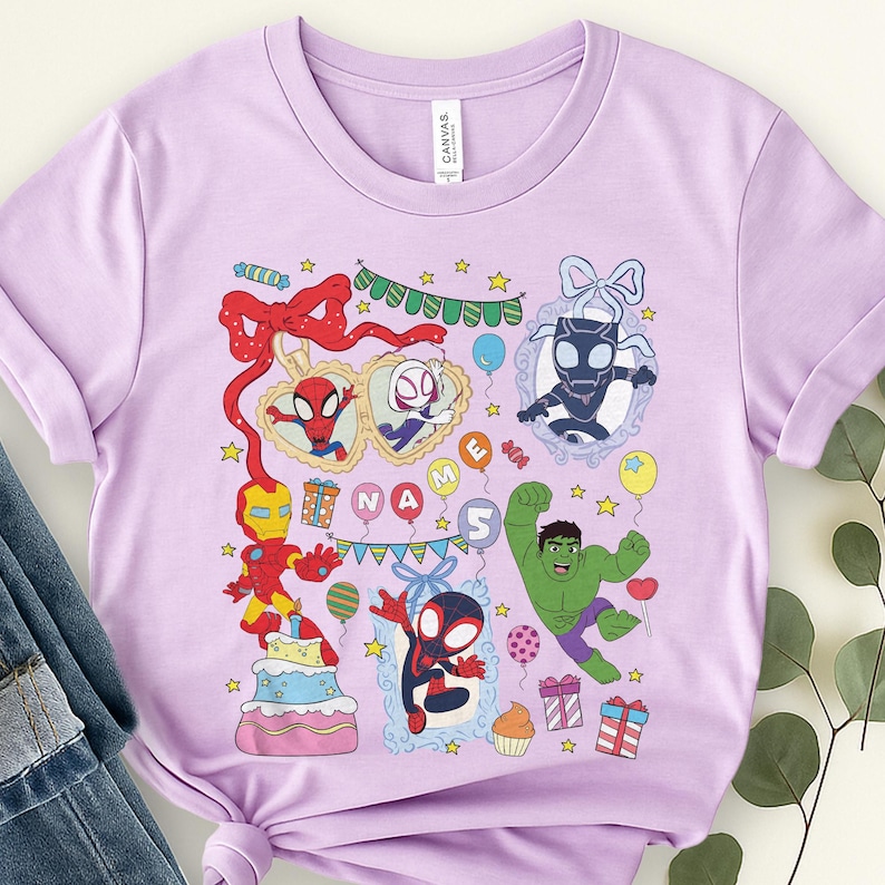 May include: A light purple short-sleeve t-shirt featuring a colorful graphic print of various superheroes, a birthday cake, presents, balloons, and stars. The design includes the text "NAME" and the number "5" surrounded by festive party elements.