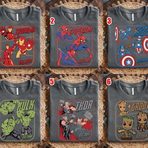 K&ouml;nnte beinhalten: Sechs graue T-Shirts mit Marvel-Superhelden-Designs. Jedes Shirt zeigt einen anderen Charakter: Iron Man, Spider-Man, Captain America, Hulk, Thor und Groot. Die Designs enthalten Charakternamen und Gr&uuml;ndungsjahre.