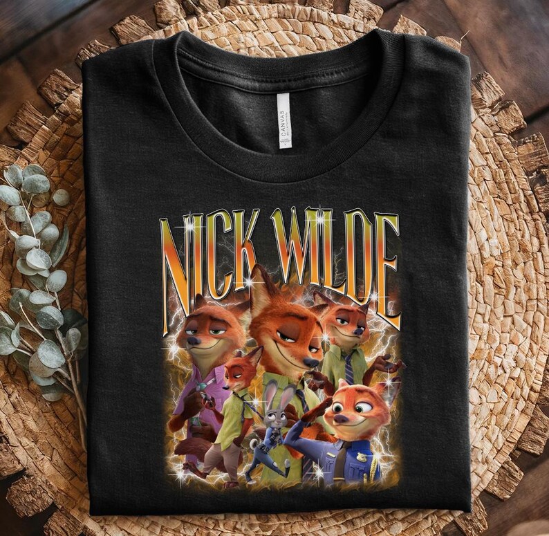 May include: Black t-shirt featuring a graphic of Nick Wilde from Zootopia. The design includes multiple images of the fox character with the text "NICK WILDE" in a stylized font. The shirt is folded on a woven surface.