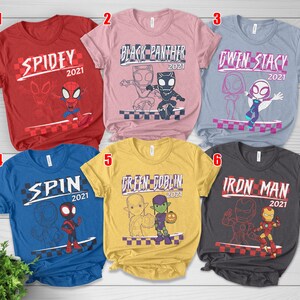 May include: Six short-sleeved t-shirts featuring Marvel characters. Each shirt has a character's name and the year "2021". The shirts are in red, pink, blue, yellow, grey, and light blue. The designs include Spidey, Black Panther, Gwen Stacy, Spin, Green Goblin, and Iron Man.