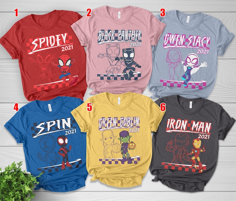May include: Six short-sleeved t-shirts featuring Marvel characters. Each shirt has a character's name and the year "2021". The shirts are in red, pink, blue, yellow, grey, and light blue. The designs include Spidey, Black Panther, Gwen Stacy, Spin, Green Goblin, and Iron Man.