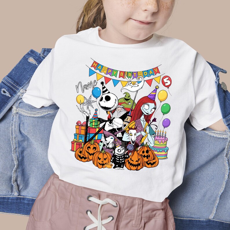 May include: White t-shirt featuring a colorful graphic of characters from The Nightmare Before Christmas, including Jack Skellington, Sally, and Oogie Boogie. The design includes pumpkins, balloons, and a birthday banner that says "Happy Birthday".