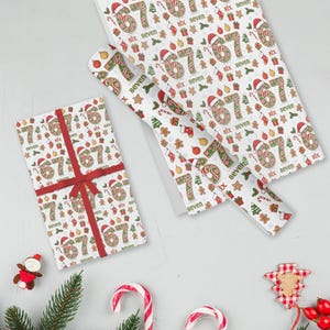 May include: White Christmas-themed wrapping paper with a repeating pattern of the numbers "67" in red and green, festive ornaments, and the words "six" and "seven." A wrapped gift with a red ribbon and bow is visible.