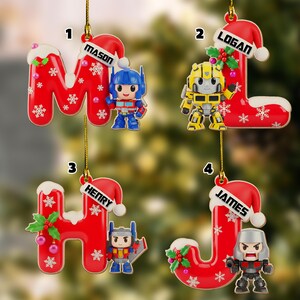May include: Christmas ornaments shaped like the letters M, L, H, and J, each with a Santa hat and a character figurine. The ornaments are red with white snowflakes and the names Mason, Logan, Henry, and James.