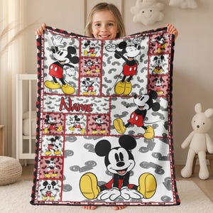 May include: A white blanket featuring a patchwork design with images of Mickey Mouse in various poses. The blanket has a red border and the word "Name" in red. The background has gray shapes.