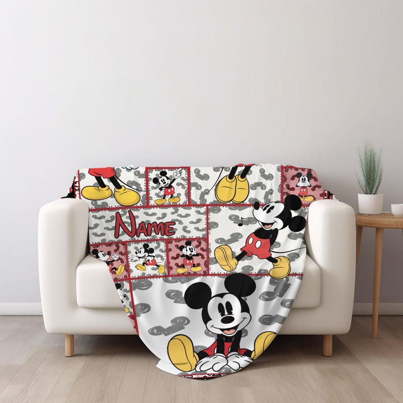 May include: A white throw blanket featuring a patchwork design with images of Mickey Mouse in various poses. The blanket has a red border and the word "Name" is displayed on the blanket.