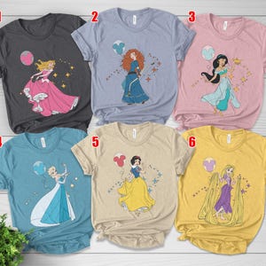 May include: Six different t-shirts, each featuring a Disney princess graphic. The shirts are in various colors, including gray, blue, pink, and yellow. Each shirt has a different princess design, with a Mickey Mouse balloon.