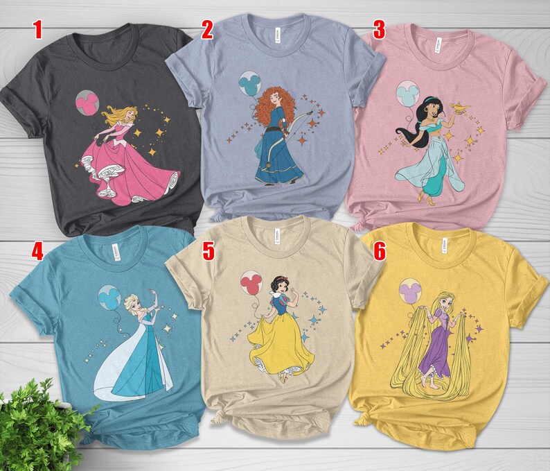 May include: Six different t-shirts, each featuring a Disney princess graphic. The shirts are in various colors, including gray, blue, pink, and yellow. Each shirt has a different princess design, with a Mickey Mouse balloon.