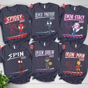 May include: Six navy blue t-shirts, each showcasing a different Marvel character. The shirts feature the character's name and the year 2021, accompanied by a graphic illustration. Characters include Spidey, Black Panther, Gwen Stacy, Spin, Green Goblin, and Iron Man.