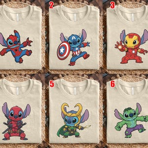May include: Six beige t-shirts with cartoon character designs. The designs include Stitch dressed as Spider-Man, Captain America, Iron Man, Deadpool, Loki, and the Hulk. The shirts are folded and displayed on a woven surface.
