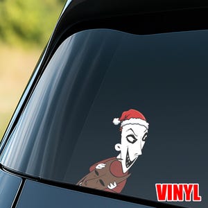 Op de afbeelding: Een vinyl sticker met een stripfiguur met een kerstmuts. Het personage heeft een wit gezicht, een sinistere grijns en draagt een rood shirt en een bruine jas. Het woord "VINYL" is in het rood gedrukt.