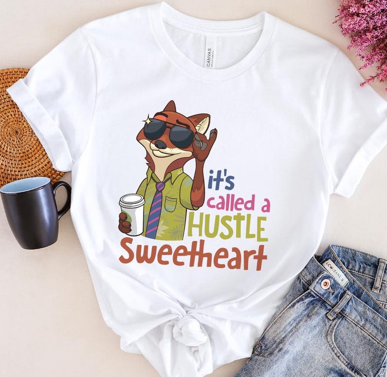 Op de afbeelding: Wit T-shirt met een cartoon vos met een zonnebril en een koffiekopje. Het shirt heeft de tekst "it's called a HUSTLE Sweetheart" in kleurrijke letters. De vos draagt een groen overhemd en een stropdas met patroon.