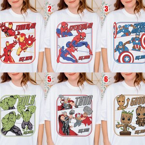 K&ouml;nnte beinhalten: Wei&szlig;e T-Shirts mit verschiedenen Marvel-Superhelden: Iron Man, Spider-Man, Captain America, Hulk, Thor und Groot. Jedes Design enth&auml;lt den Namen der Figur und ein Gr&uuml;ndungsjahr in einem rechteckigen Rahmen.