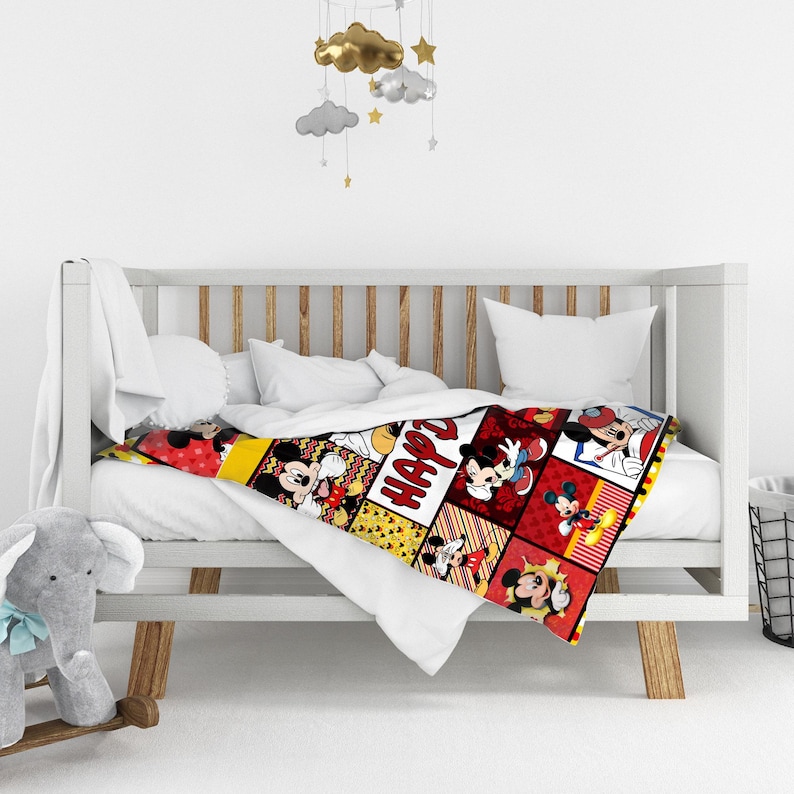 Pu&ograve; includere: Una colorata coperta per bambini con un design patchwork con immagini di Topolino in varie pose. La coperta ha uno schema di colori rosso, giallo e nero, con la scritta "HAPPY" stampata sopra. &Egrave; drappeggiata su una culla bianca.